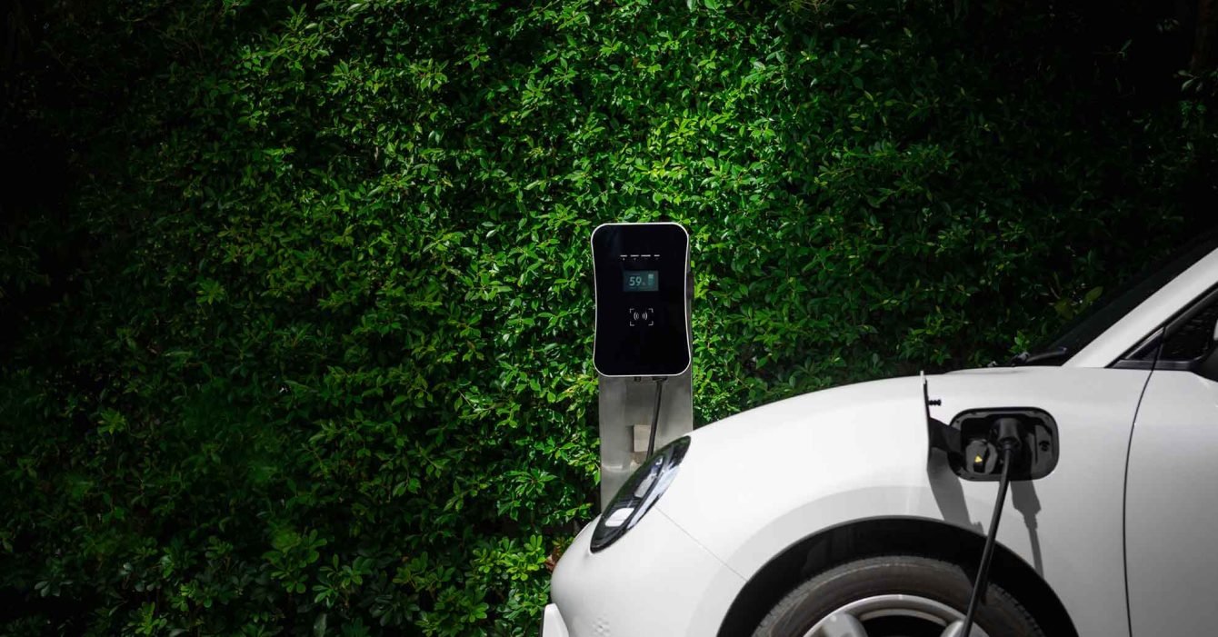 side-view-progressive-ev-car-with-charging-station-green-foliage-background