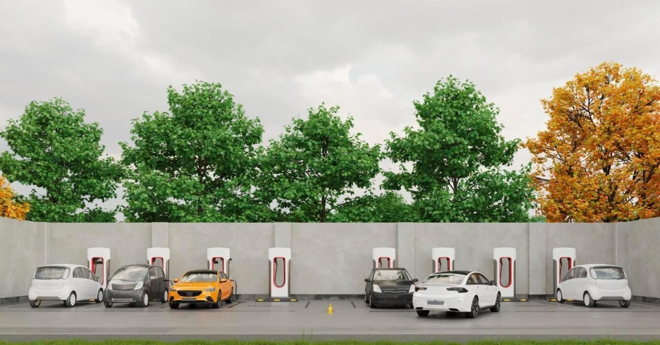 Saudi EV infrastructure 2025: A parking area with electric vehicle chargers, featuring a variety of cars, set against green trees and an autumn backdrop.