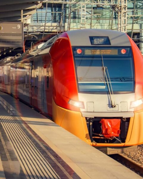 Micromobility in Saudi Arabia: A modern, streamlined train with a red front is parked at a station under an overhead sign indicating Track 9.